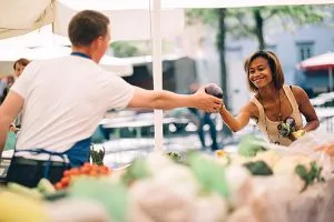 Young woman buying vegetables at farmers market